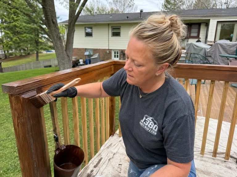 Worker brushing wood stain onto deck railings and balusters