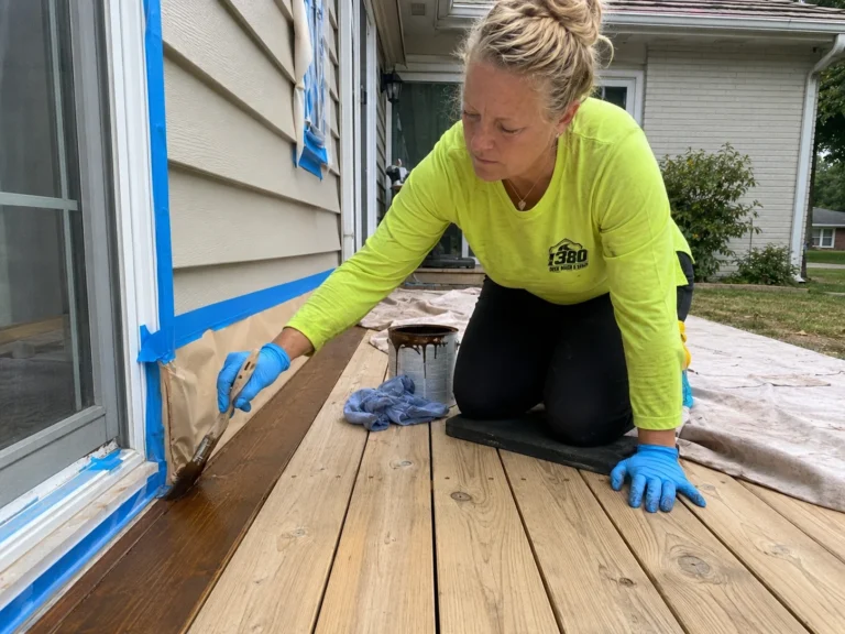 Worker brushing deck stain along boards beside exterior siding