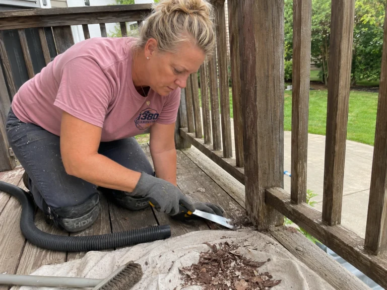Worker hand scraping loose old stain from the edge of a deck railing