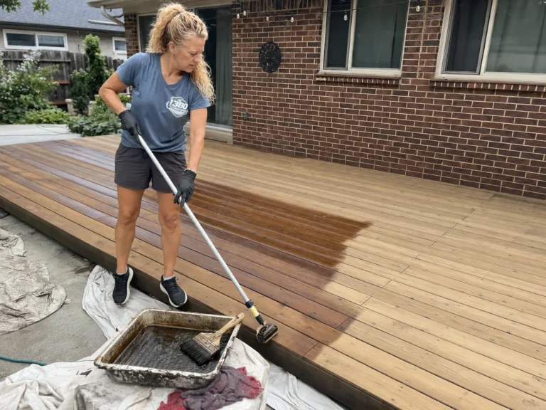 Worker rolling brown stain across a large wood deck floor