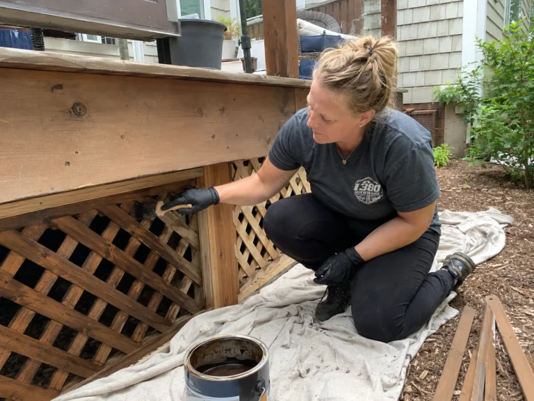 Worker brushing stain onto deck lattice and fascia boards